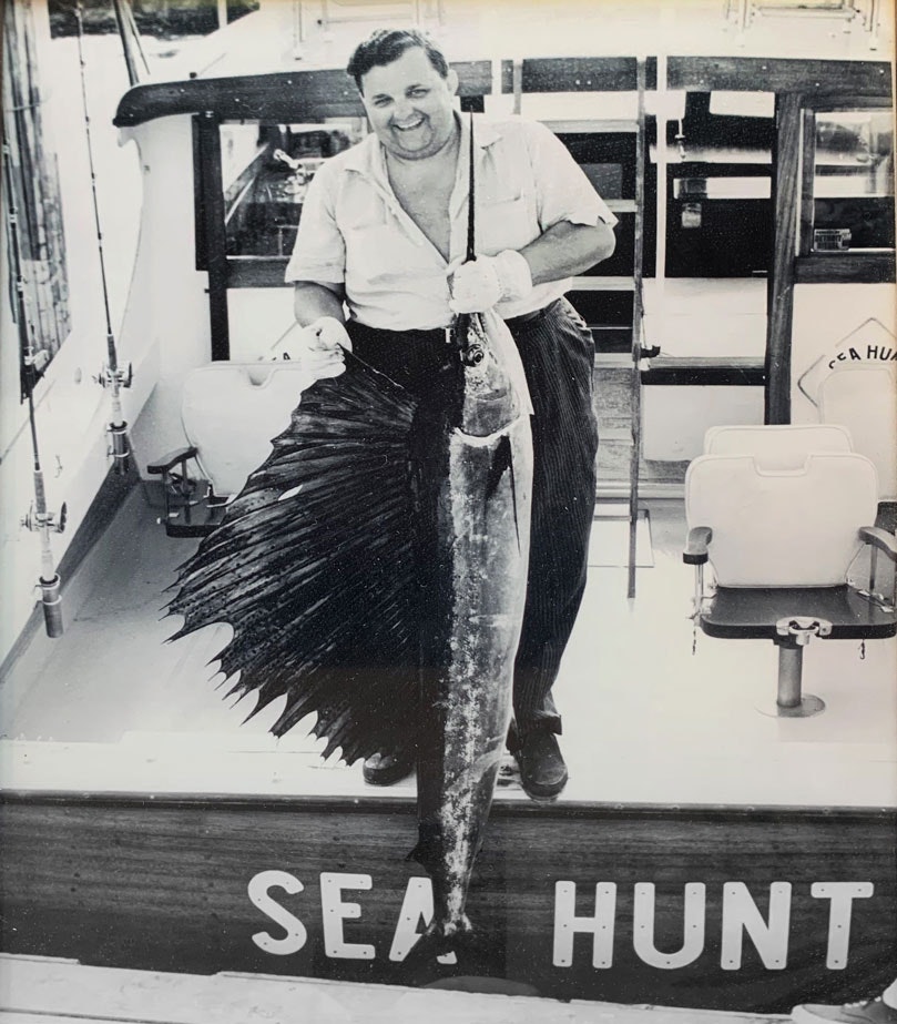 black and white photo of a man holding a marlin he caught