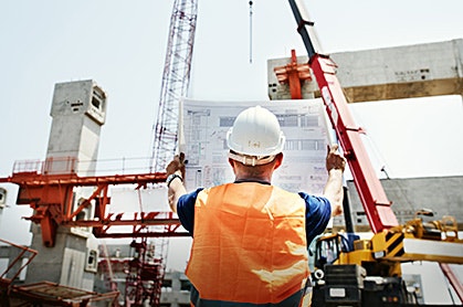 construction worker holding up a blueprint in front of a building under construction